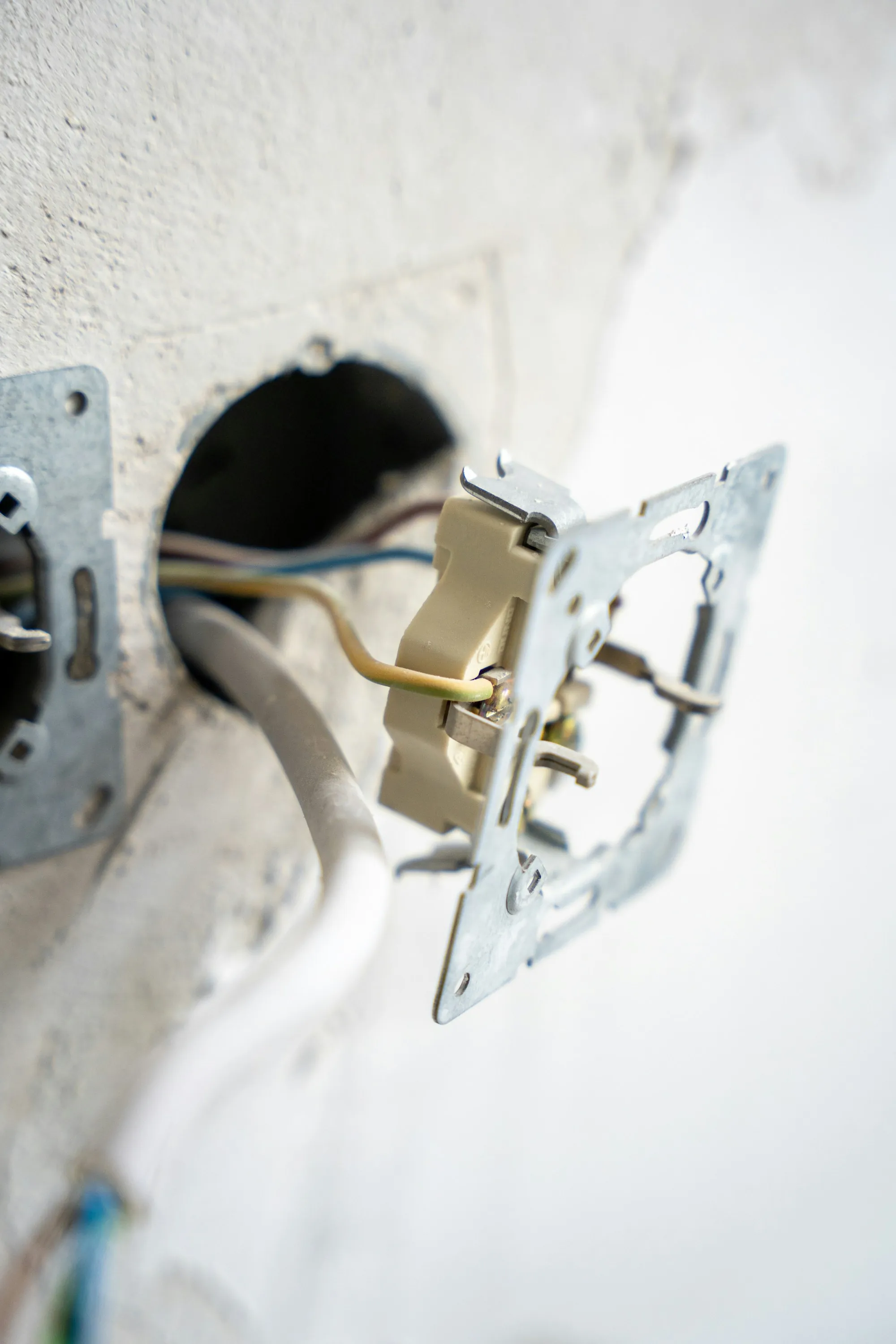 Electrician kneeling to fit a switch box into a freshly drilled wall